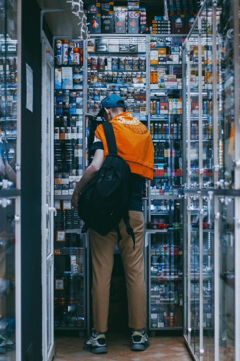 Adult man with backpack browsing electronics in a narrow store aisle.